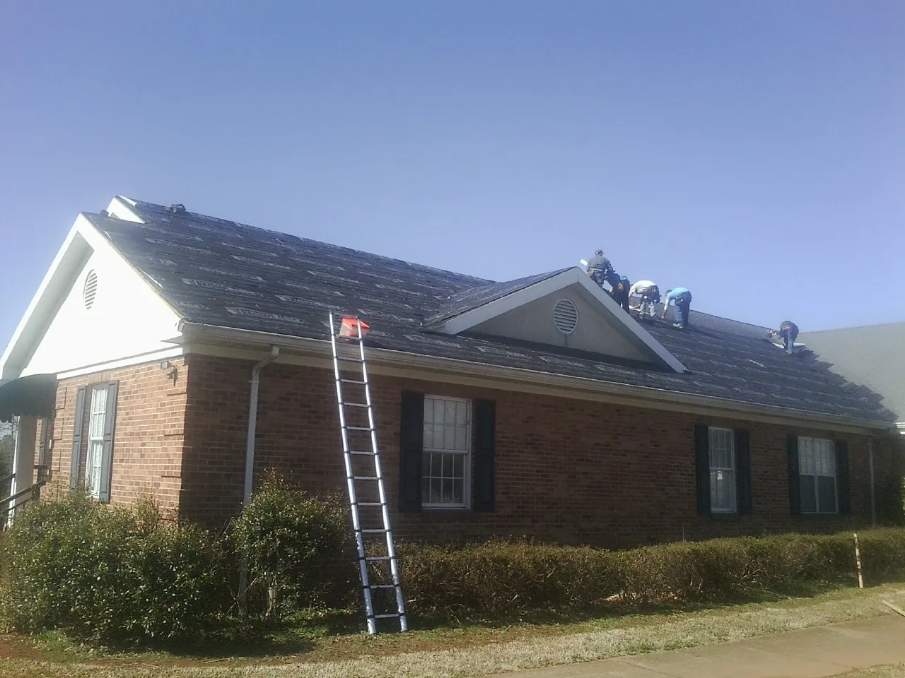 Crew tearing shingles off a brick ranch roof with a ladder set — Emergency Roof Repair work by our crew in Brinkhaven