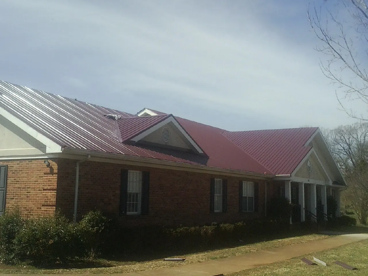 Red metal roof with gabled entries on a long brick building, from a Hail Damage Roof Repair job in Brinkhaven