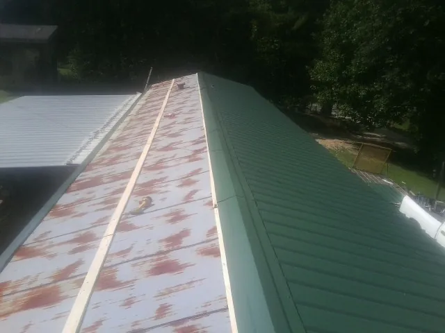 Old rusted panels beside newly installed green metal roofing — Wind Damage Roof Repair by Roofing Brothers in Brinkhaven