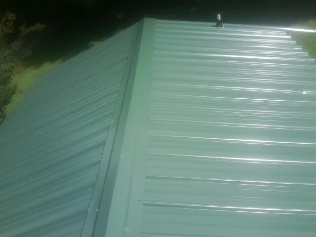 New green metal panels meeting at the ridge of a roof — Flat Roof Repair work by our crew in Brinkhaven