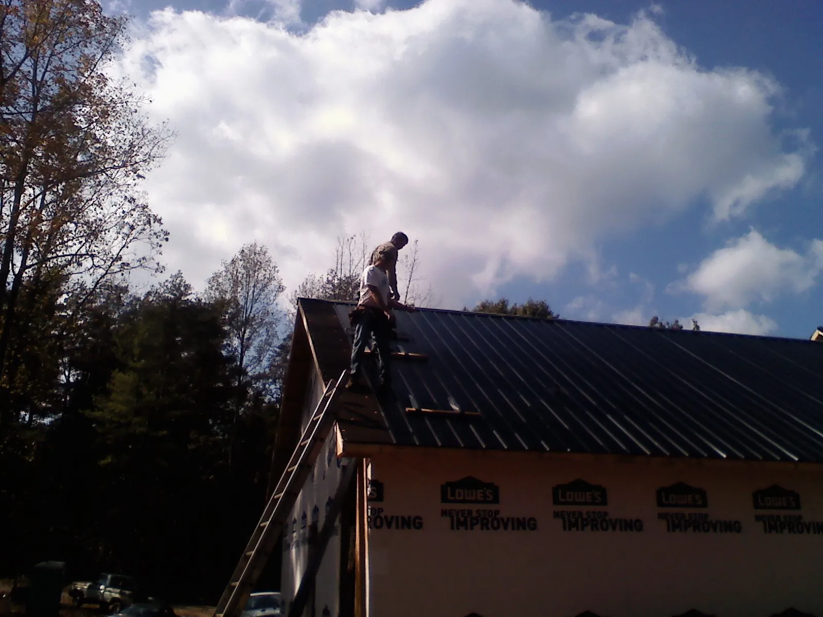 Roofer fastening dark metal panels high against a cloudy sky, from a Roof Inspection job in Brinkhaven