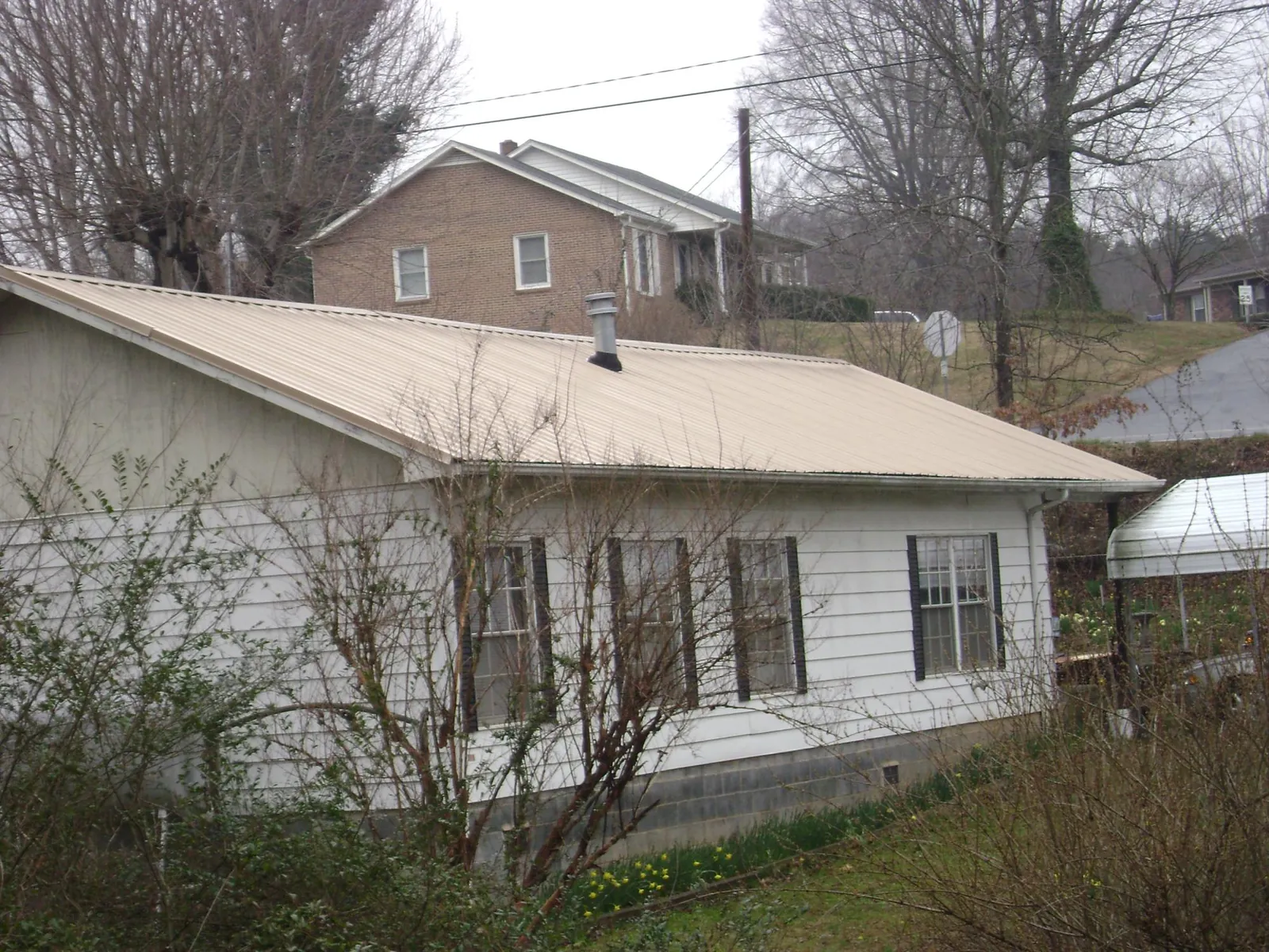 Tan metal roof on a white sided house set into a hillside — Commercial Roofing by Roofing Brothers in Brinkhaven